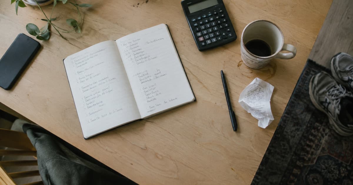 Un bureau avec un carnet, une calculatrice et des baskets, pour préparer ses tarifs