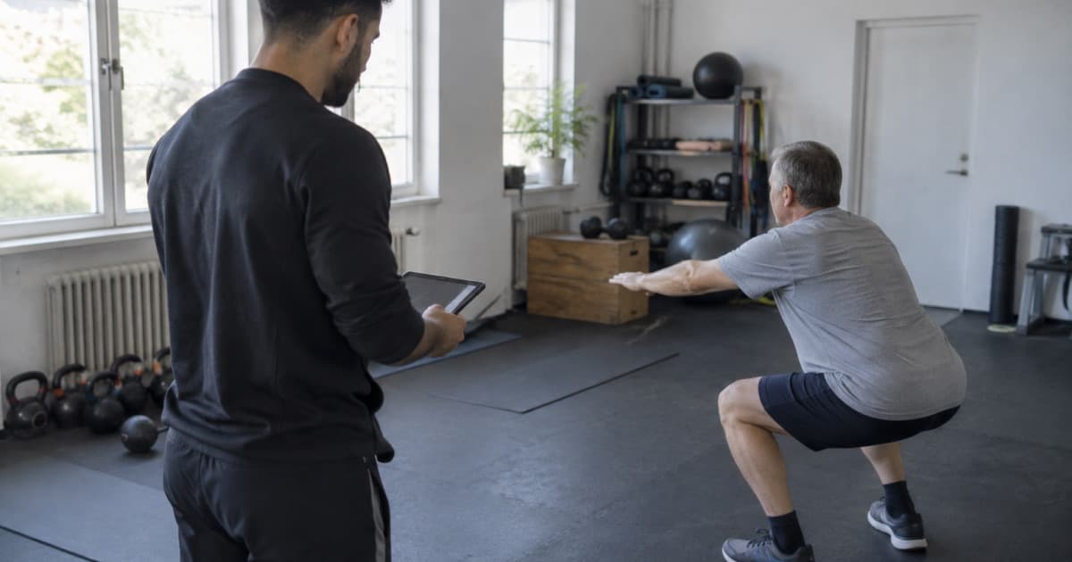 Un coach guide un client débutant sur un squat dans un studio lumineux